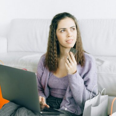 Young woman sitting with laptop and credit card, surrounded by shopping bags, reflecting online shopping lifestyle.