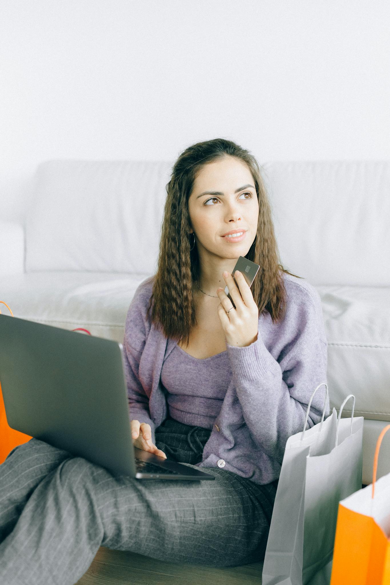 Young woman sitting with laptop and credit card, surrounded by shopping bags, reflecting online shopping lifestyle.